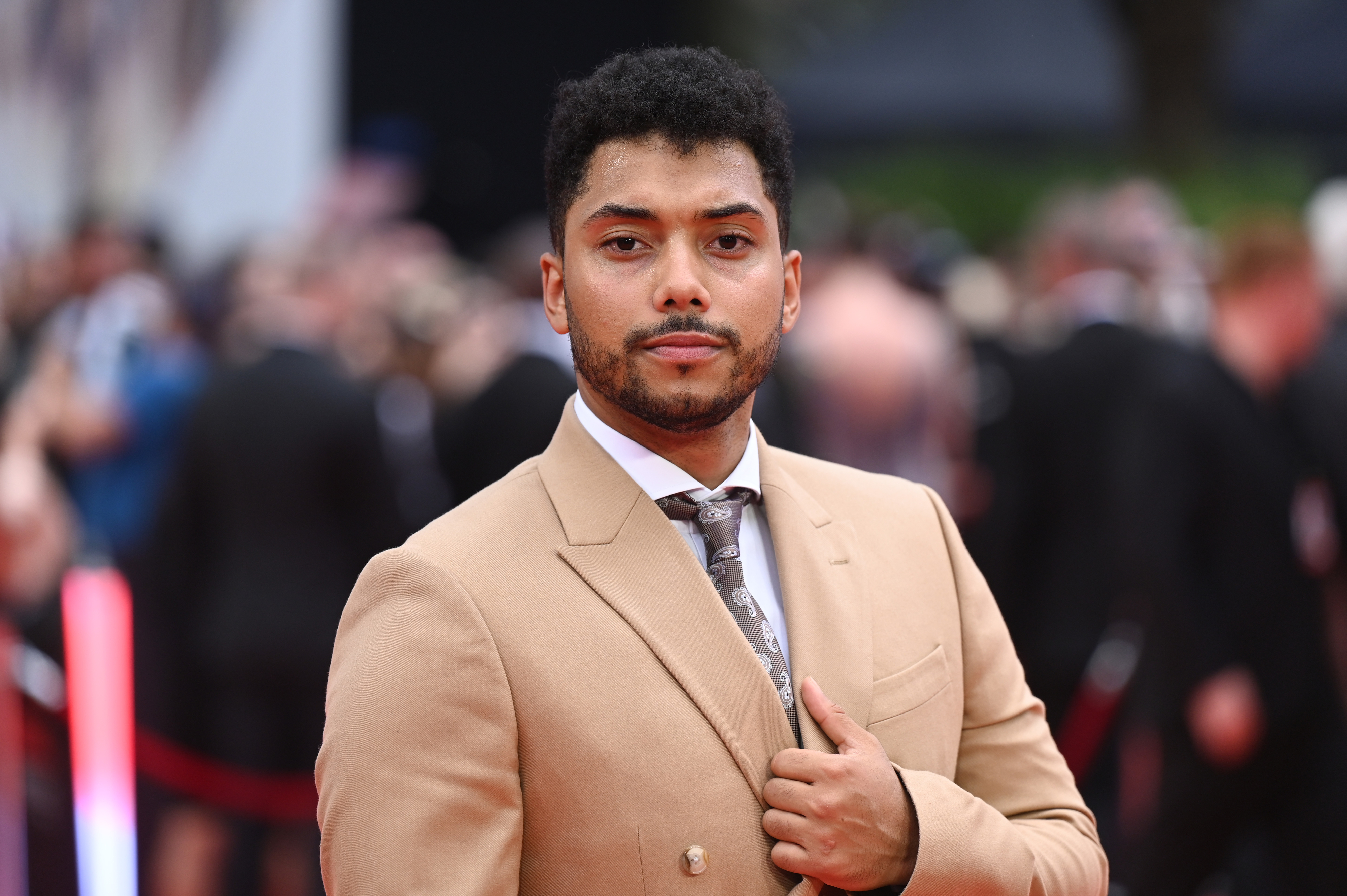 Chance Perdomo in a tailored suit and tie stands on the red carpet with his hand on his lapel