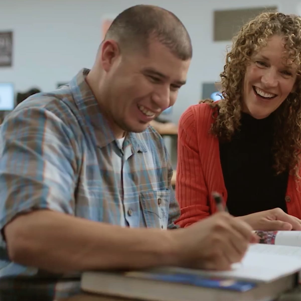A man and a woman are smiling and looking at a piece of paper that the man is writing on