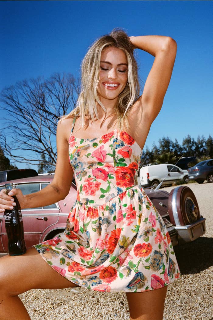 model in floral dress holding a Coke bottle beside a vintage car
