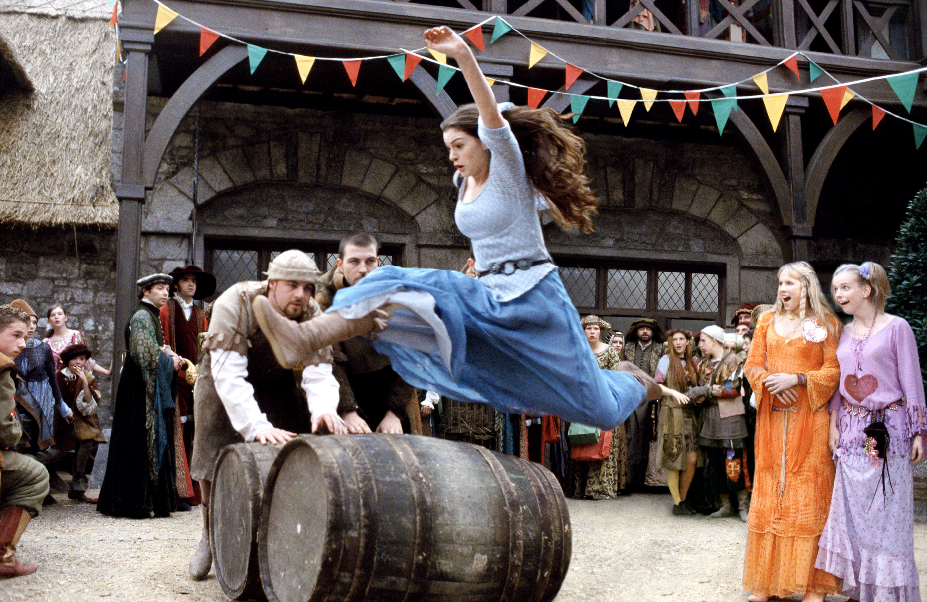 Ella in medieval attire leaps over a barrel at a fair; spectators watch in background