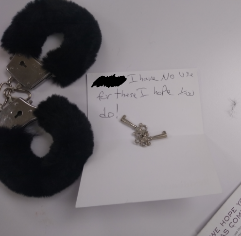 Handcuffs with fake fur and a note reading &quot;I have no use for these I hope you do!&quot; on a white surface