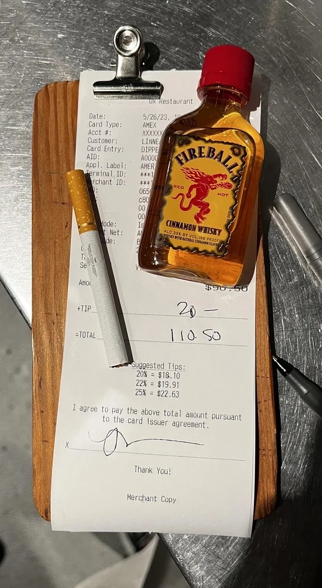 A restaurant bill with a tip calculated and a mini bottle of Fireball Whiskey and a cigarette left as a tip