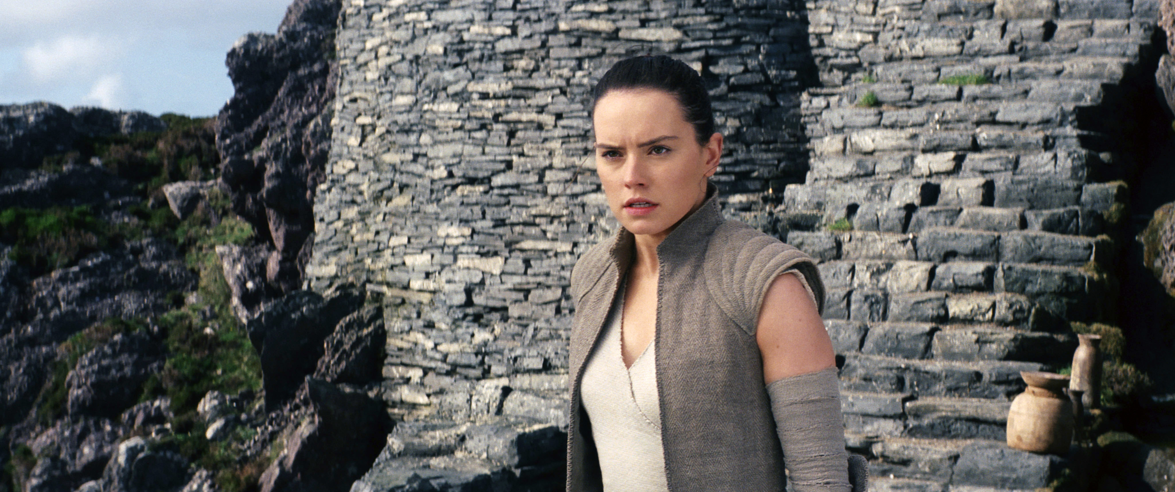Rey from Star Wars stands in front of a stone wall