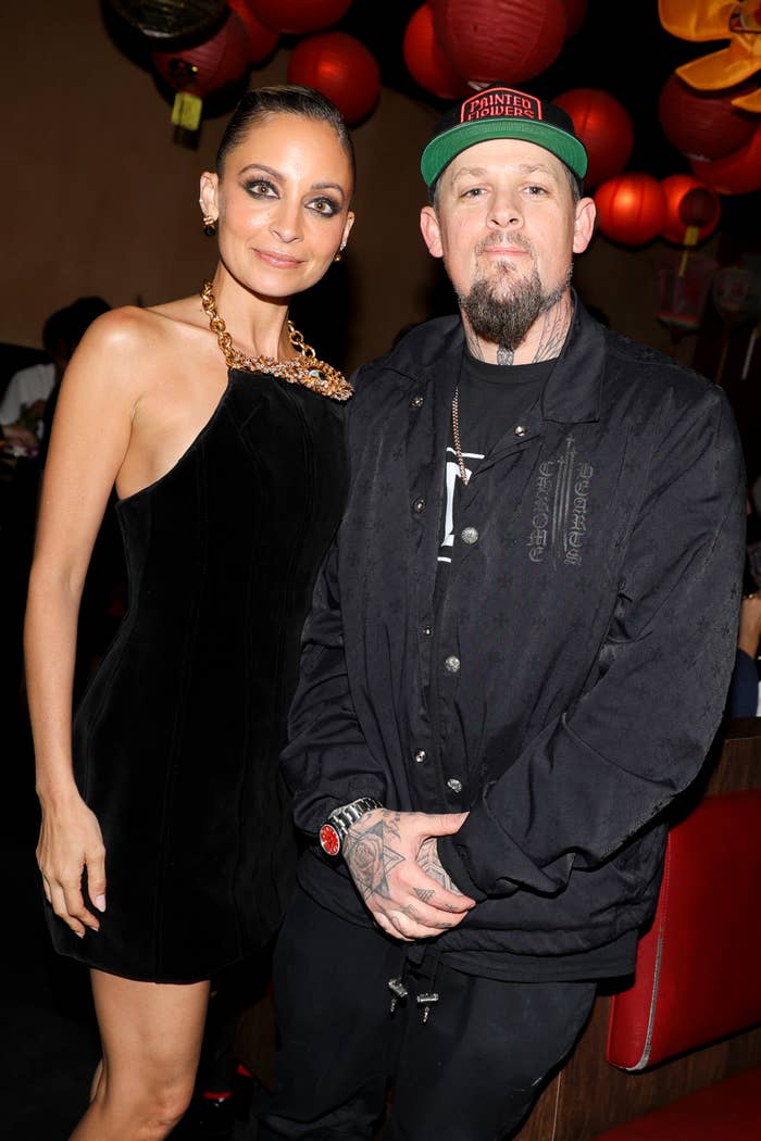 Nicole Richie in a velvet dress and Benji Madden in a graphic jacket and cap, posing together at an event
