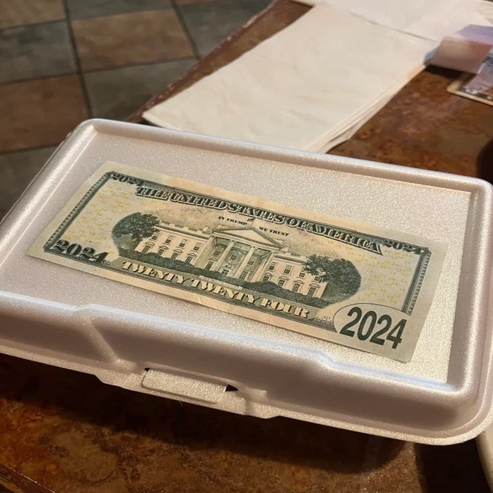 A foam container with a "2024" bill printed on top sits on a table