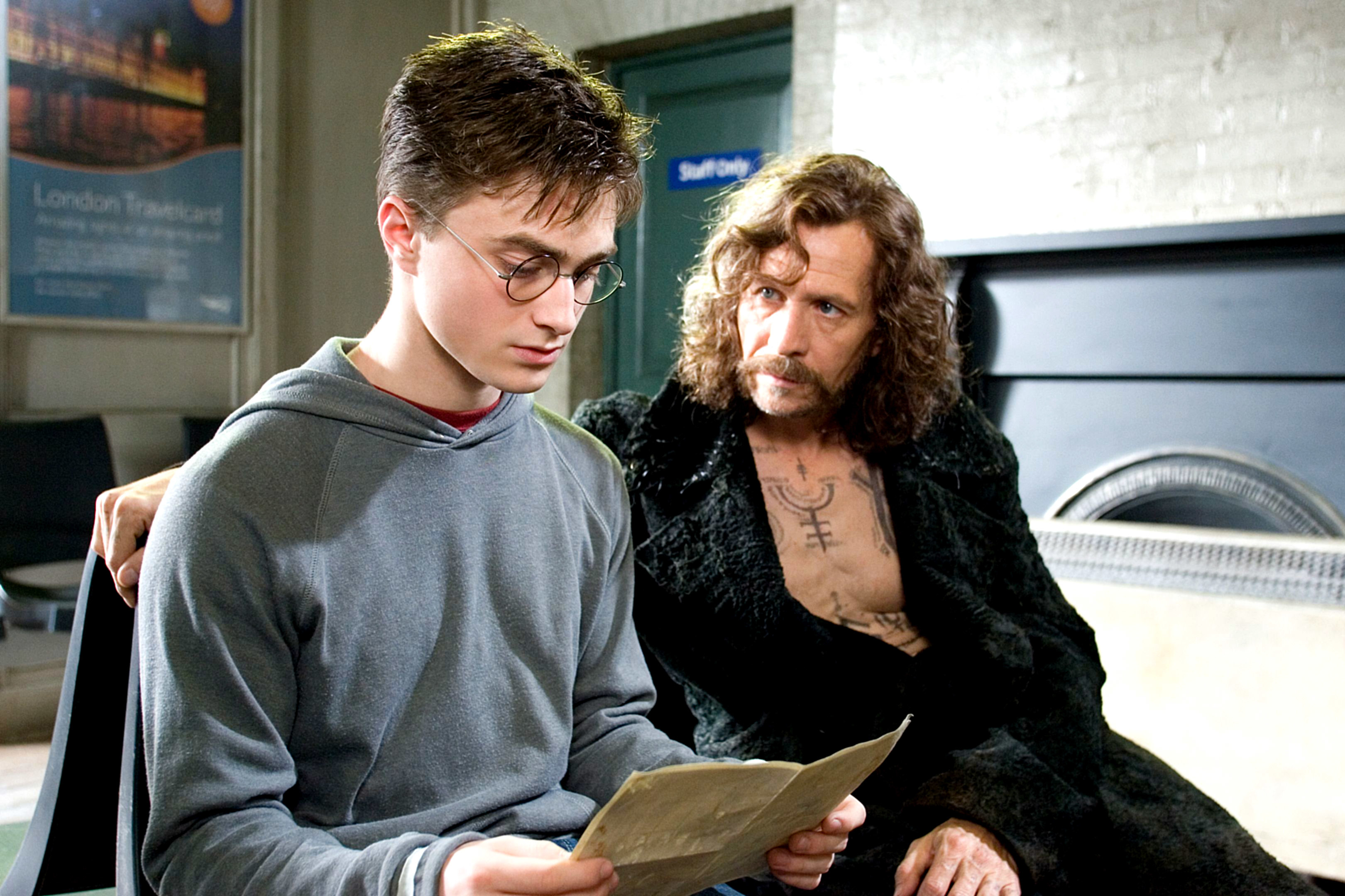 Harry Potter and Sirius Black looking at a document inside a dim room. Sirius wears a dark, textured coat