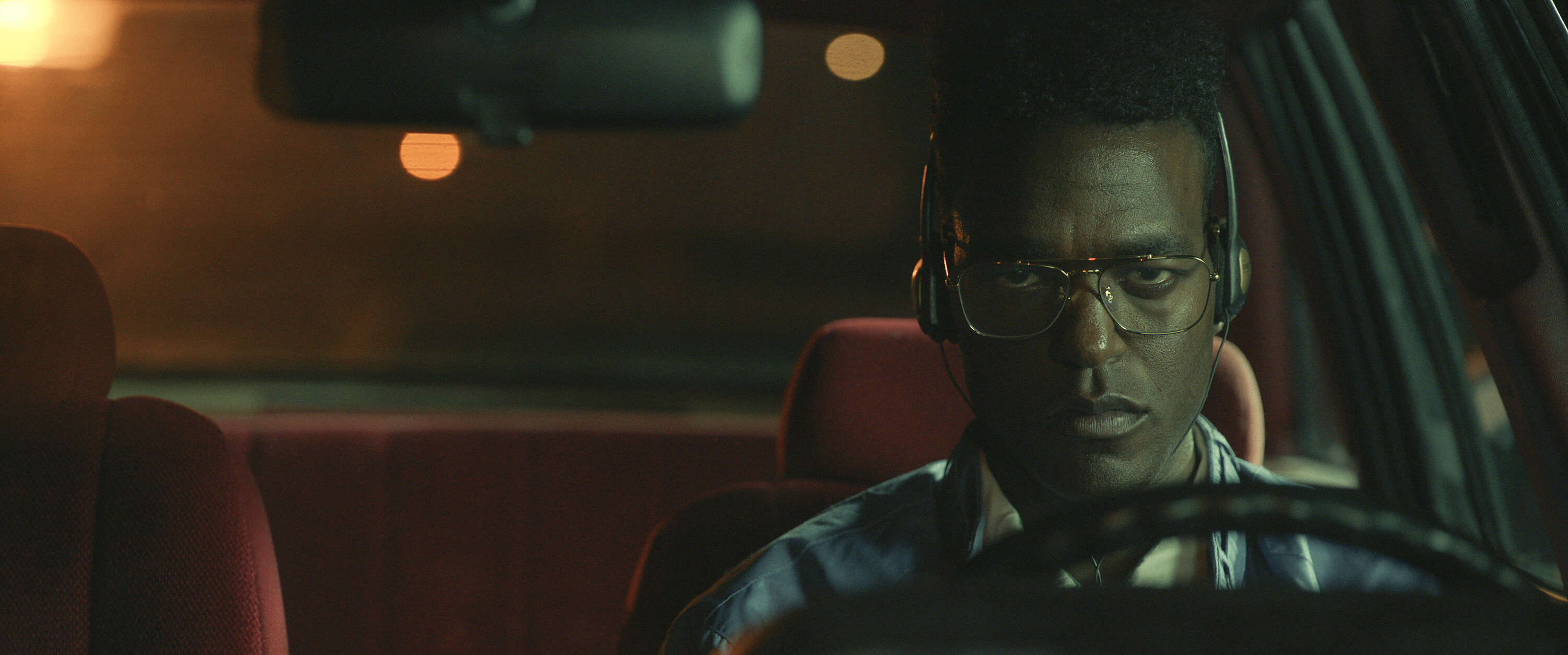 Man with glasses focused on driving at night, intense expression, interior car scene