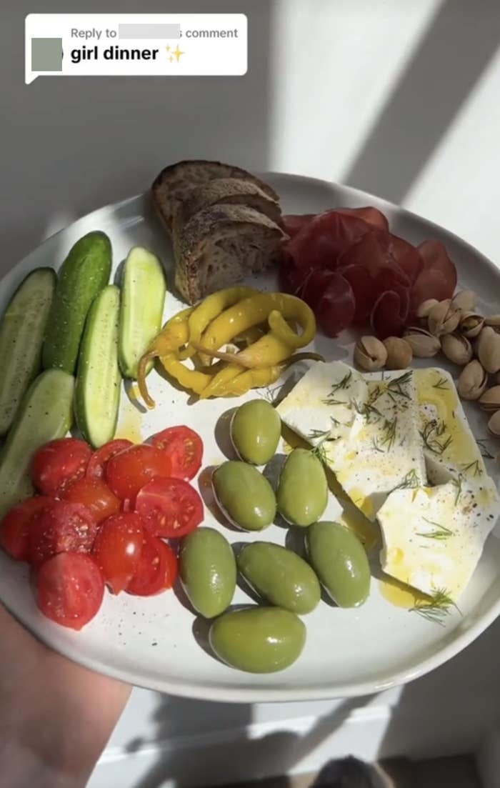 A plate with an assortment of food: cucumber slices, tomatoes, olives, cheese, nuts, bread, and sliced meats