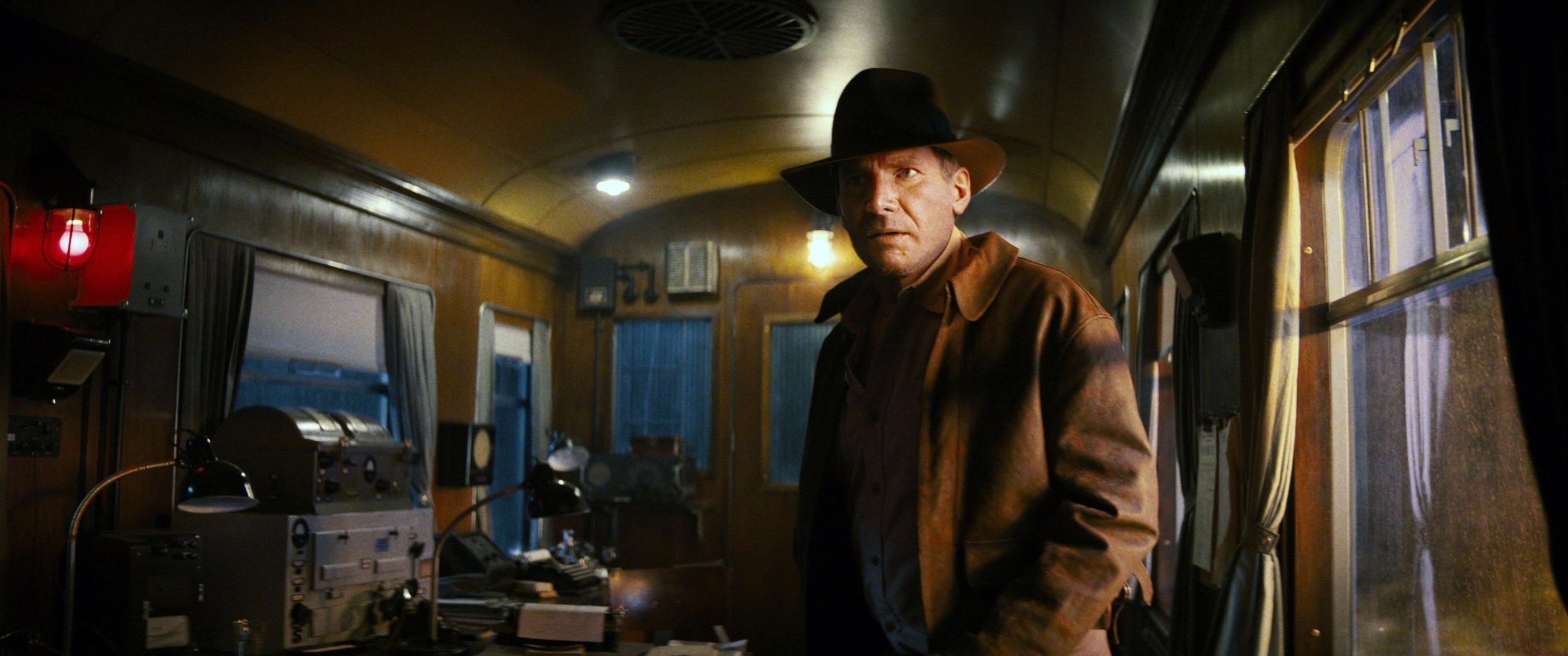 Indiana in a fedora and trench coat inside a vintage train car