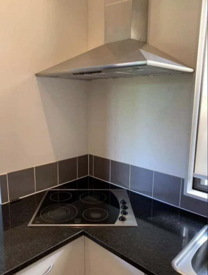 Corner kitchen area with a stove top directly under an angled extractor hood