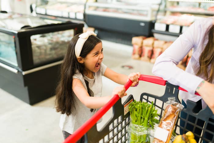 A joyful child with a shopping cart laughs during grocery shopping with a parent