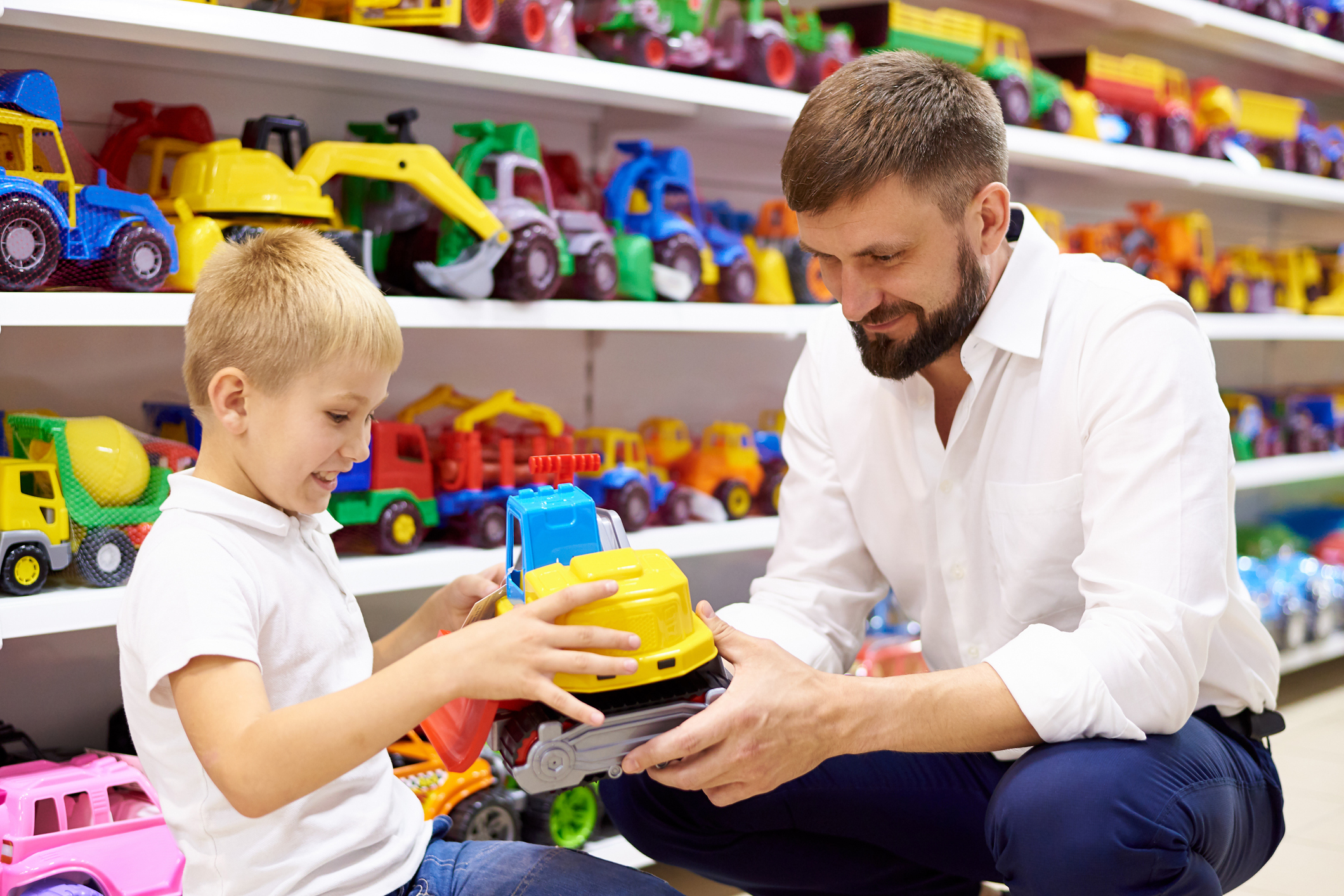 Adult and child smiling, examining a toy truck together in a toy store aisle