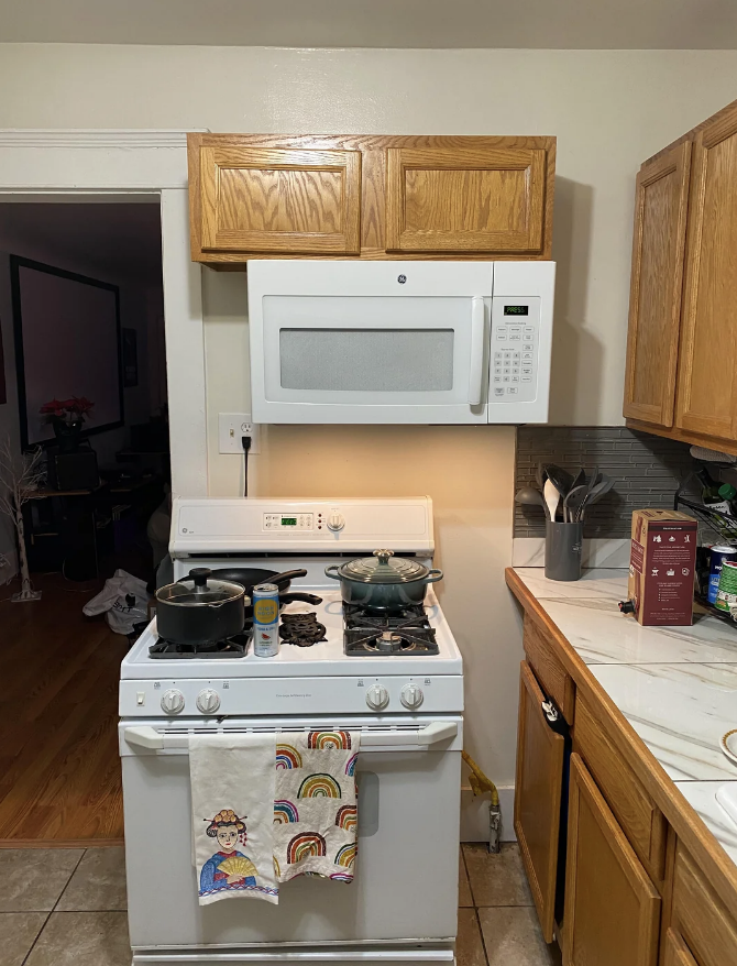 A kitchen with a microwave above a stove, pots on the stove, and a towel hanging on the oven door