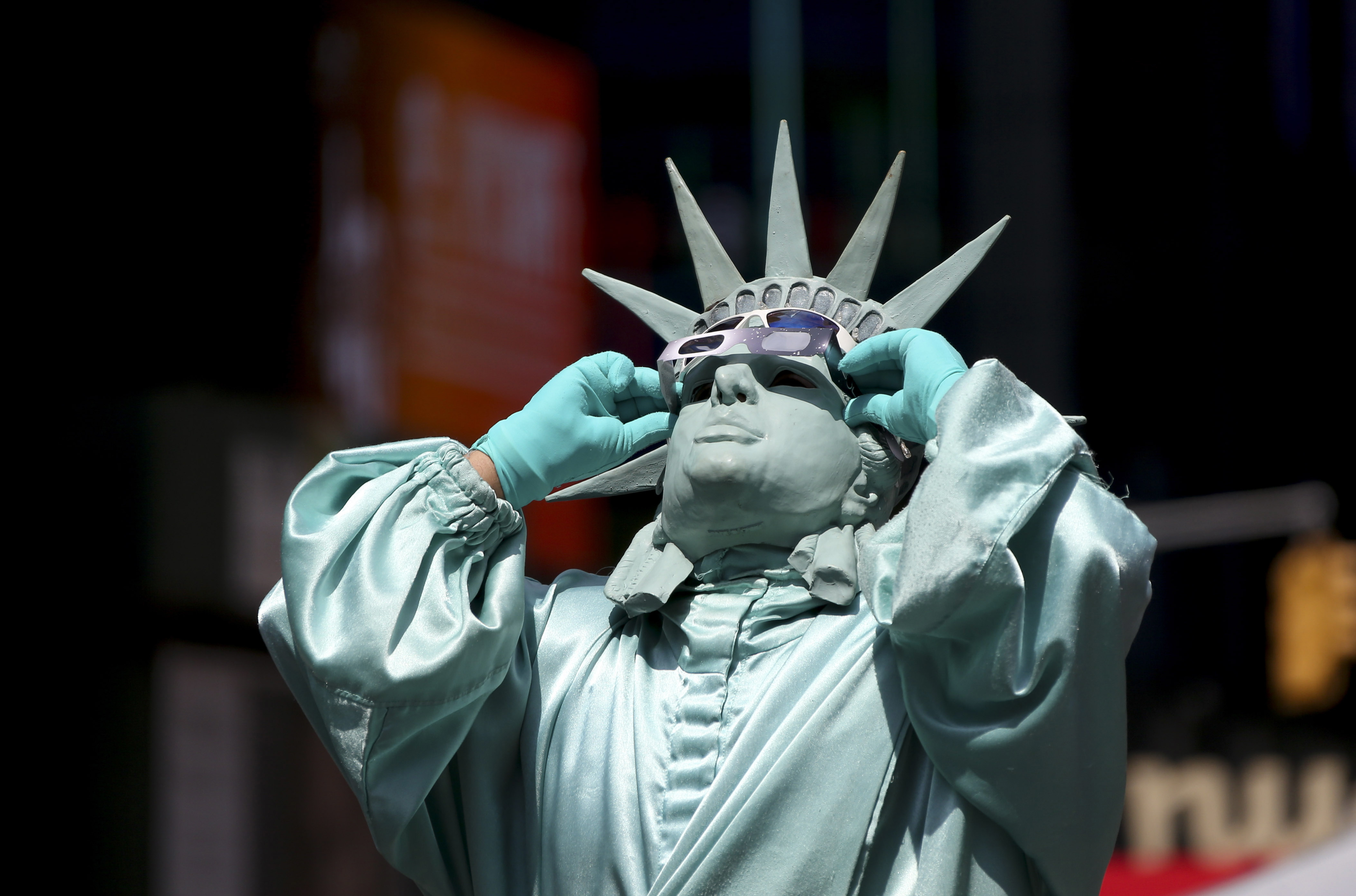 Person dressed as the Statue of Liberty with sunglasses adjusting their crown