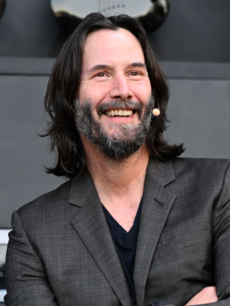 Keanu Reeves smiling in a gray suit at an event