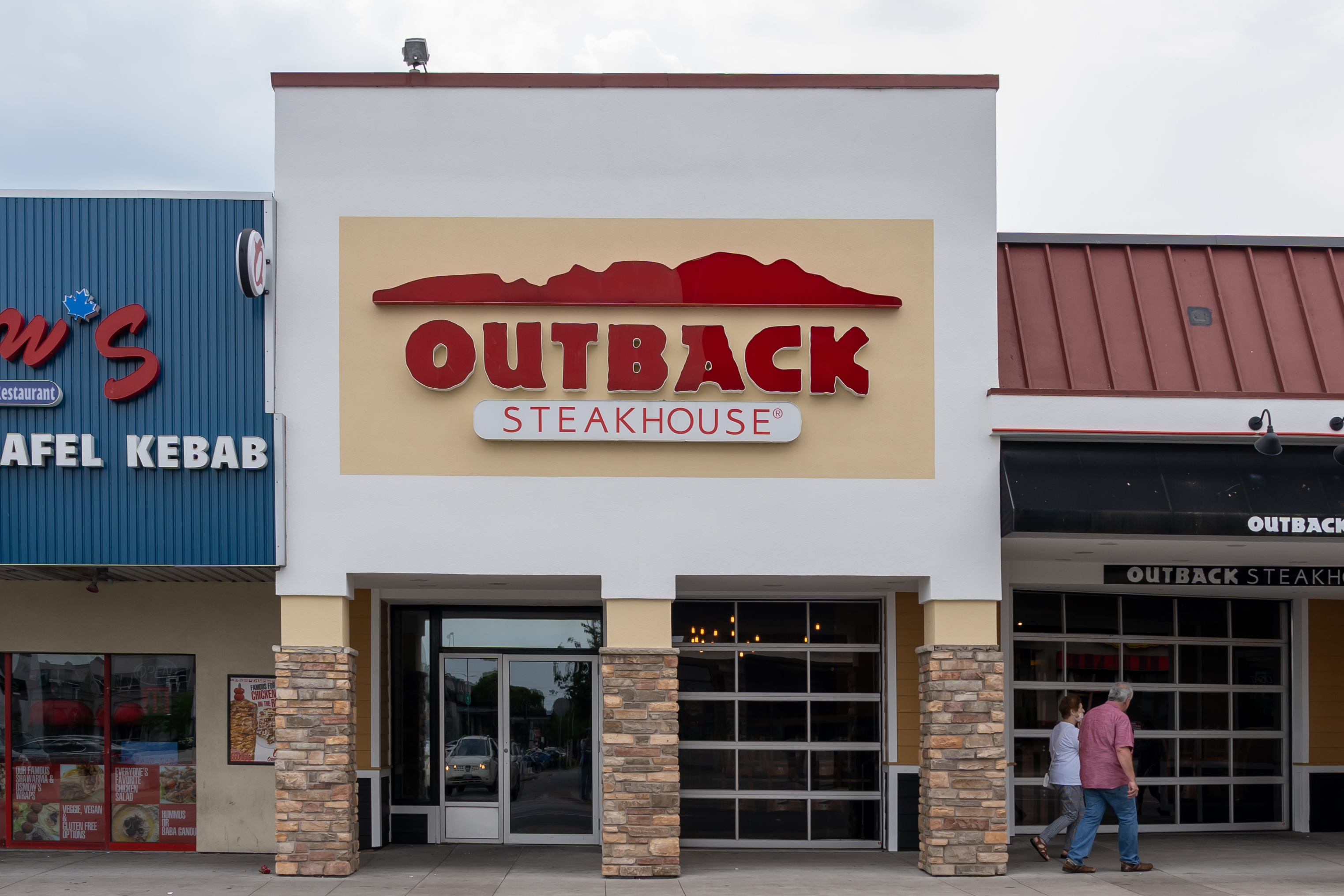 Facade of Outback Steakhouse with two people walking by, suitable for a travel dining feature