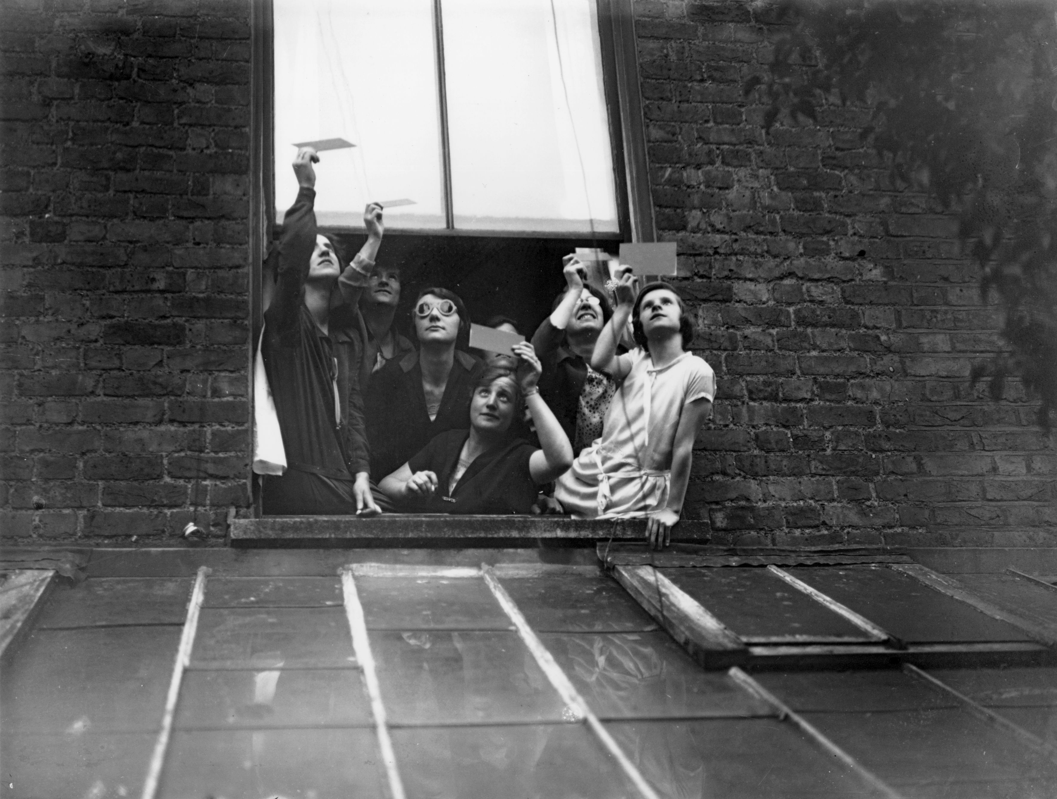 Group of people looking out a window, raising hands upward, with expressions of anticipation or excitement