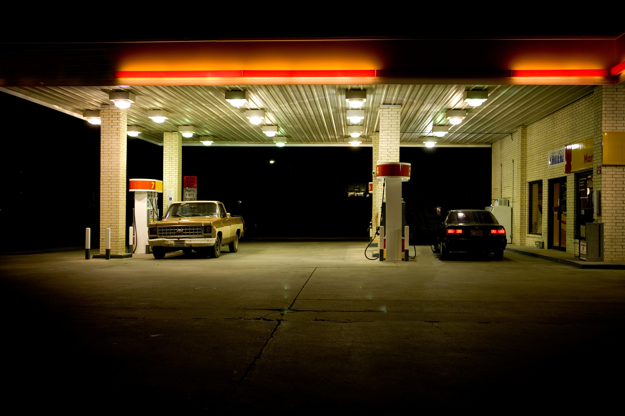 A gas station at night with illuminated canopy, two cars parked by the pumps
