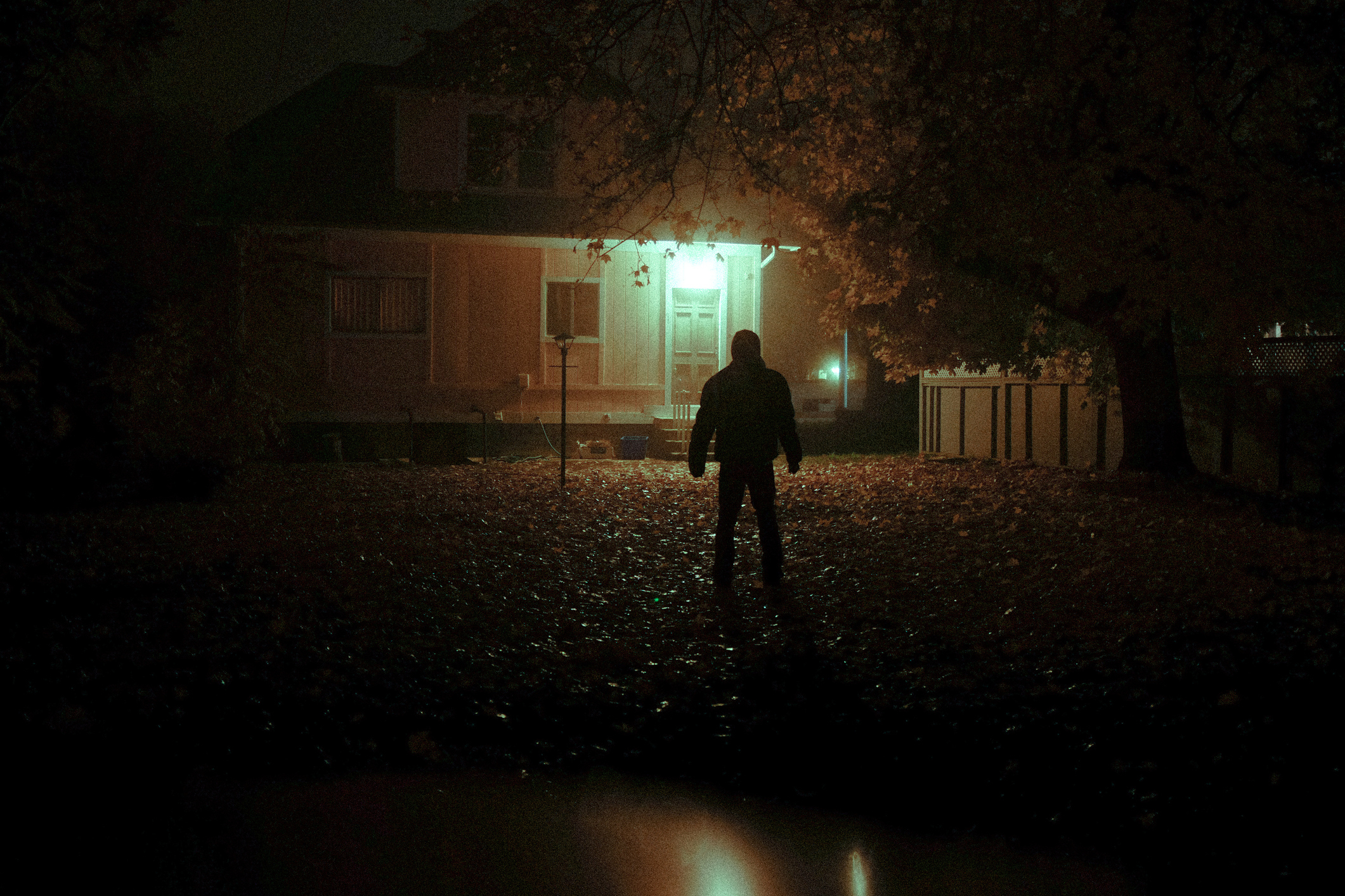 Person standing in front of a house at night, illuminated by a single light source
