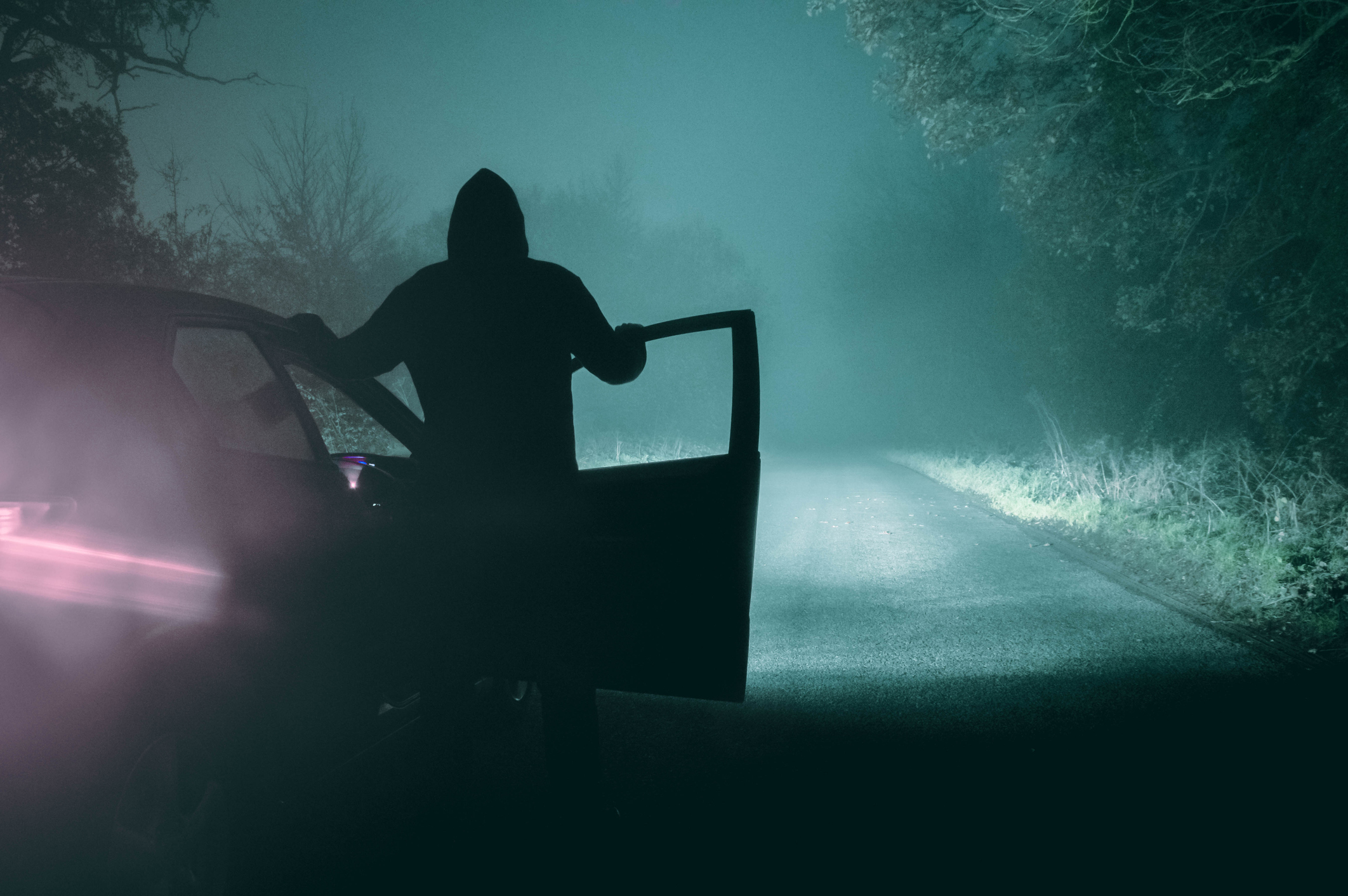 Silhouetted person getting into a car at night with fog surrounding the area
