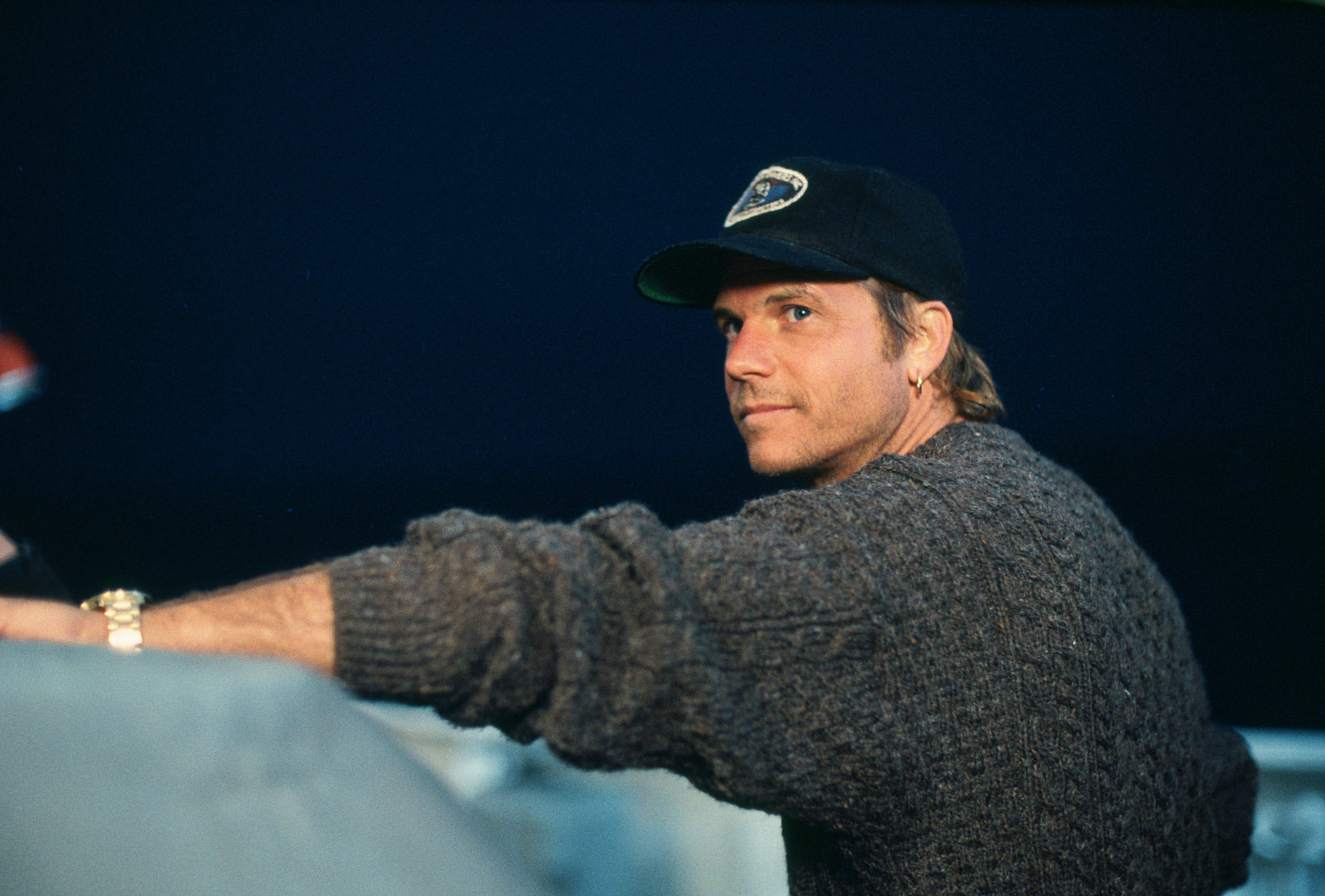 Man in knit sweater and baseball cap looking over shoulder, casual attire