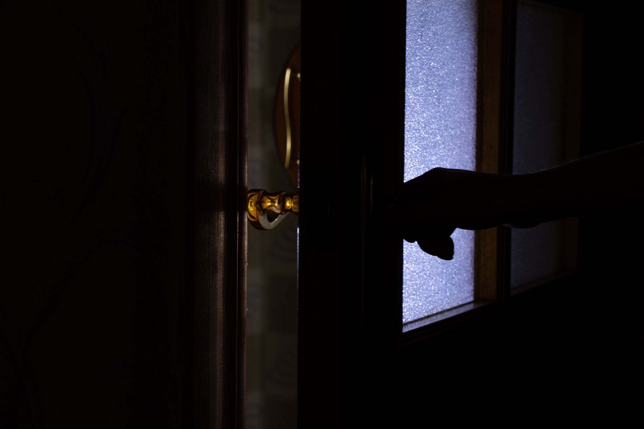 A silhouetted hand is opening a door slightly, allowing light to enter a dark room