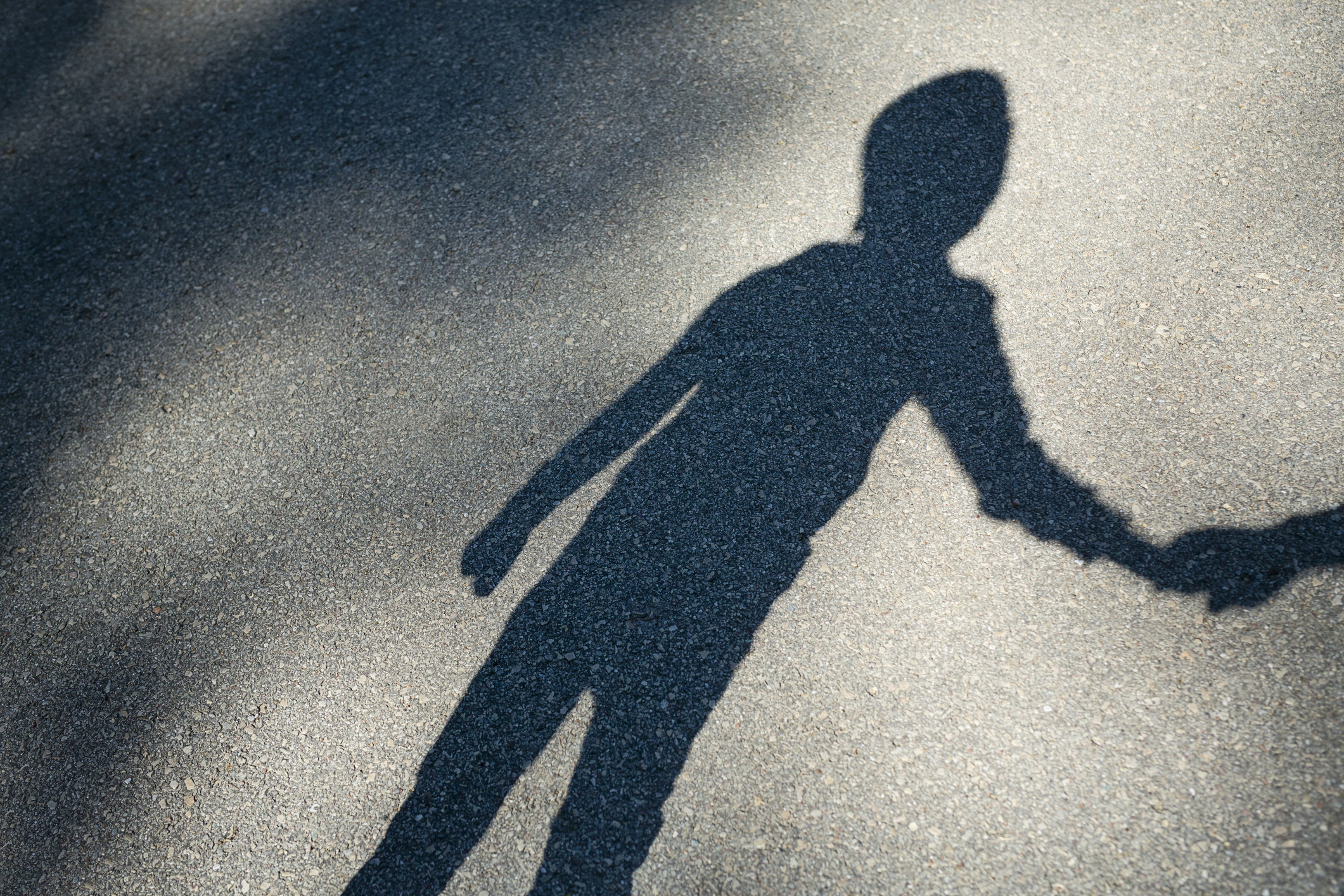 Shadow of a person on pavement, holding hands with a child&#x27;s shadow