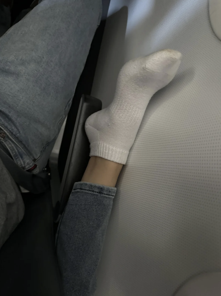 Person&#x27;s sock-covered foot wedged between airplane seats, humorously appearing hand-like