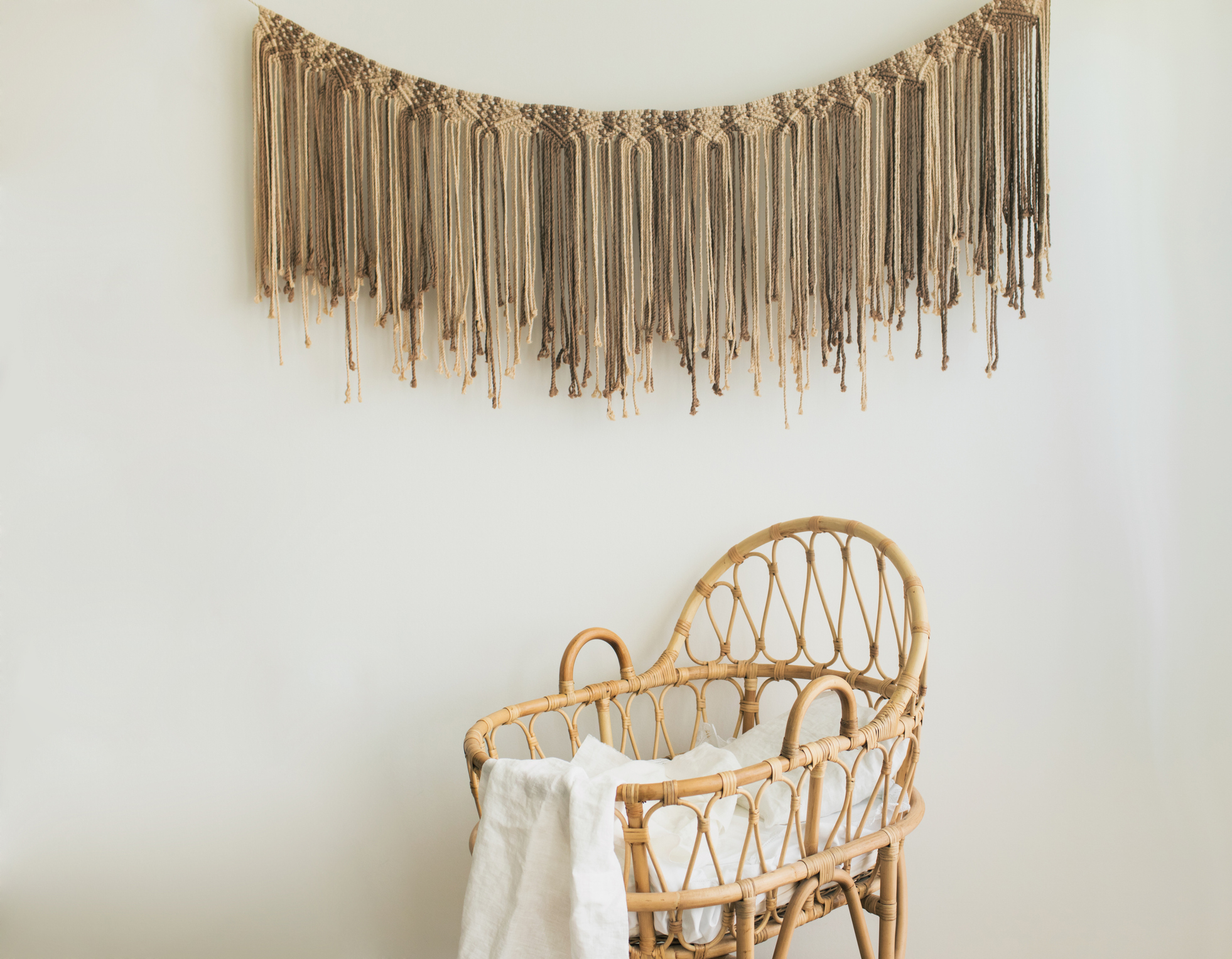 Woven wall hanging above a wicker bassinet with a blanket, in a nursery setting