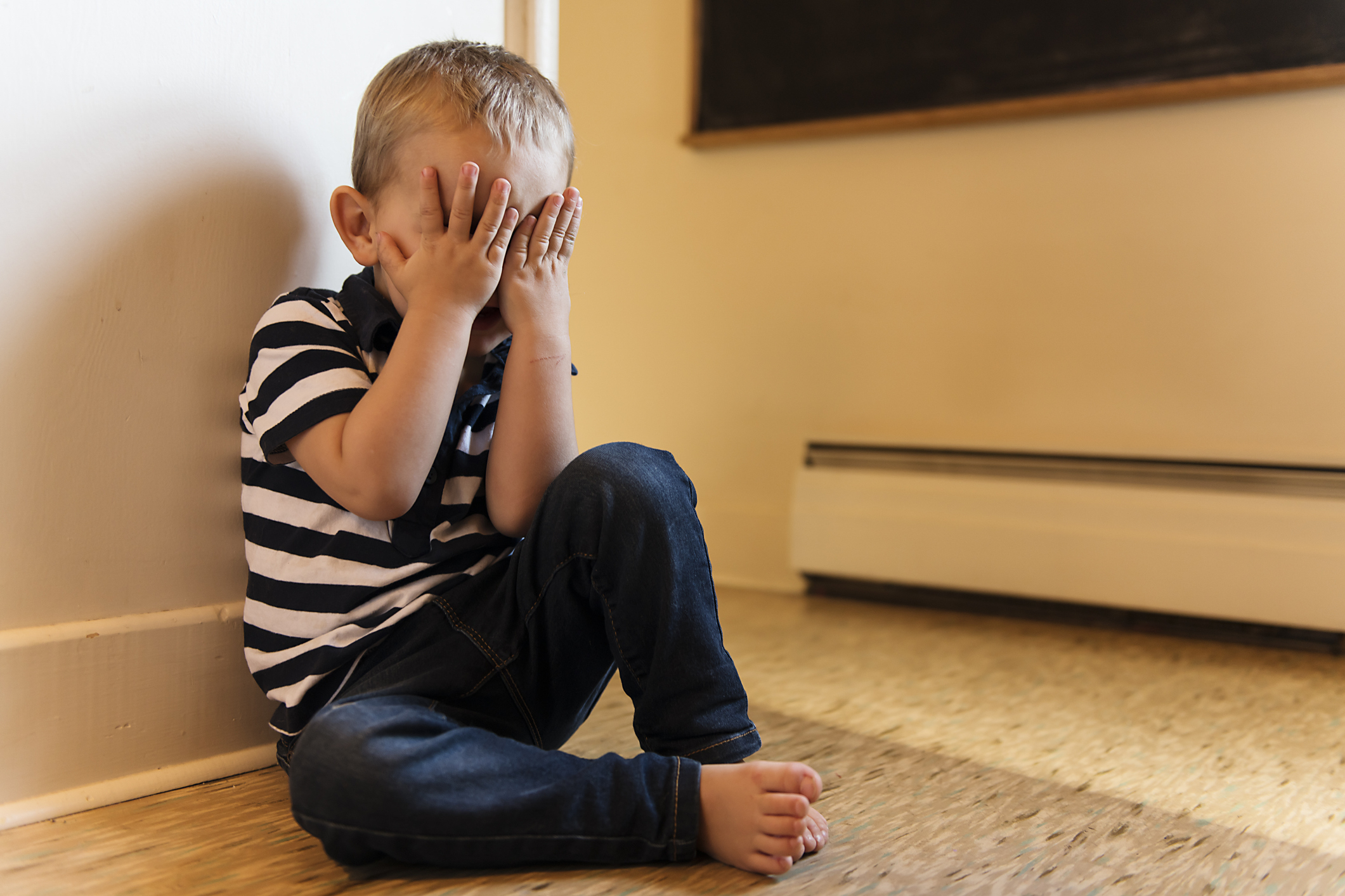 Child sitting on floor with hands covering face, appears upset or playing hide and seek