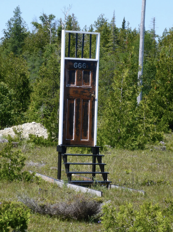 An isolated door with stairs and a &quot;666&quot; sign, standing in a natural landscape