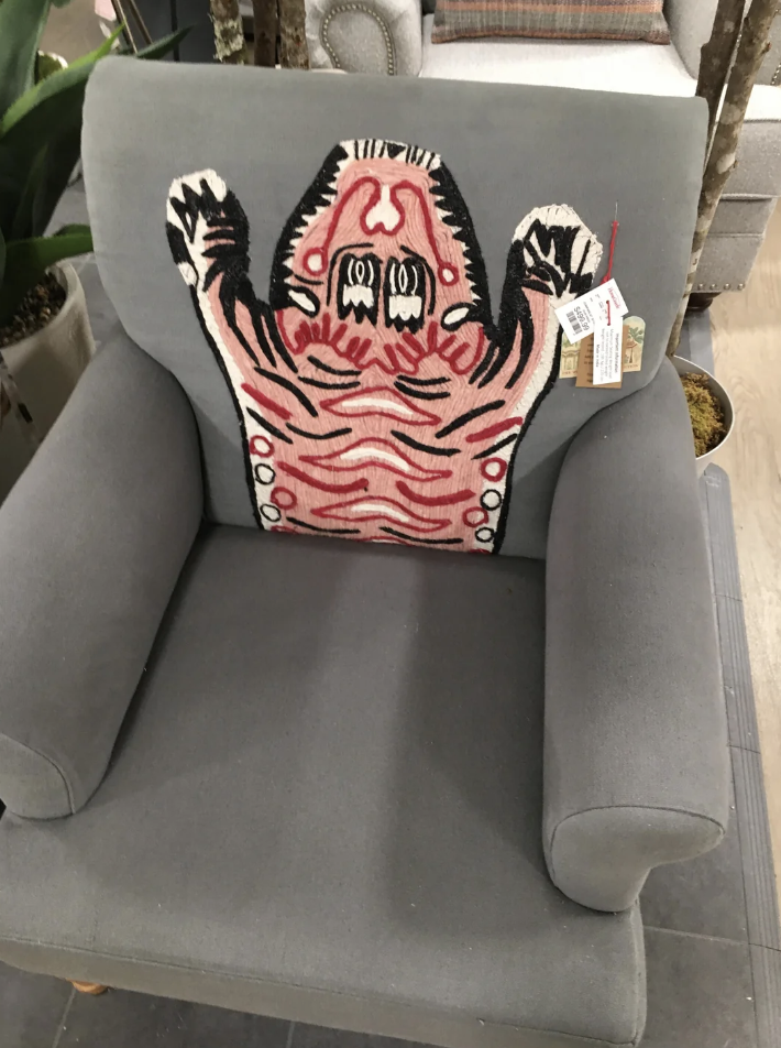 Decorative cushion with a quirky monster design placed on a grey armchair in a store setting