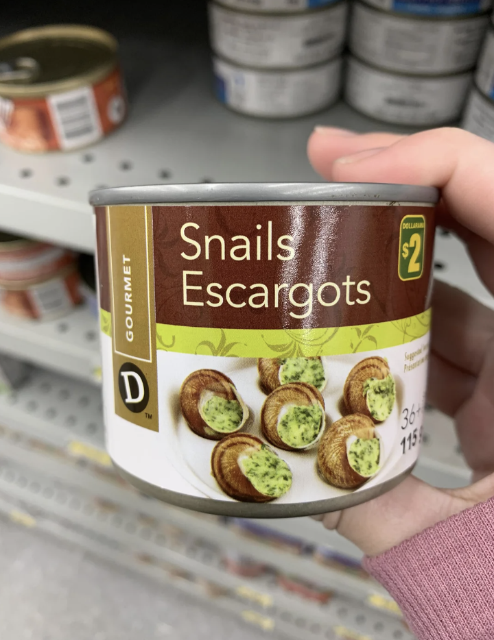 Hand holding a can labeled &quot;Snails Escargots&quot; on a store shelf; price tagged at $2