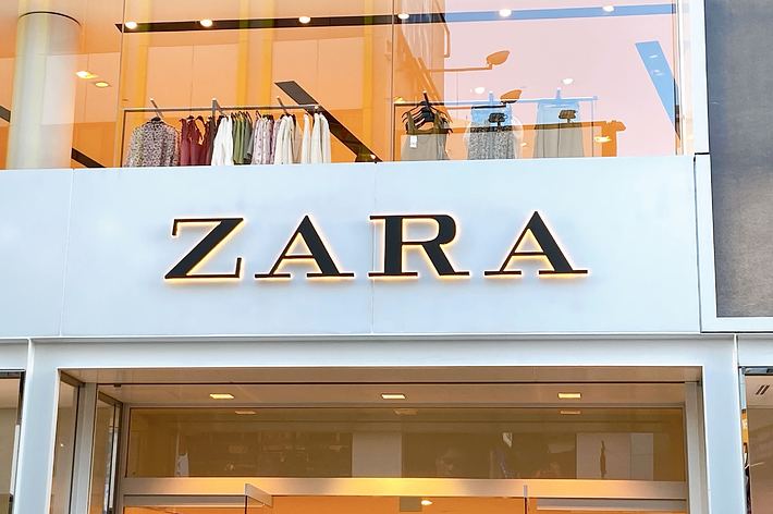 Storefront sign for ZARA with clothing items displayed in the window behind