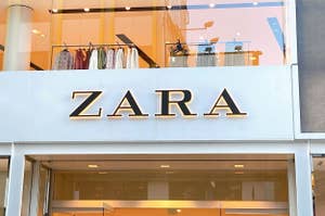 Storefront sign for ZARA with clothing items displayed in the window behind