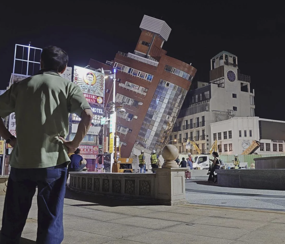 Person observing a tilted building at night, creating an optical illusion of falling over