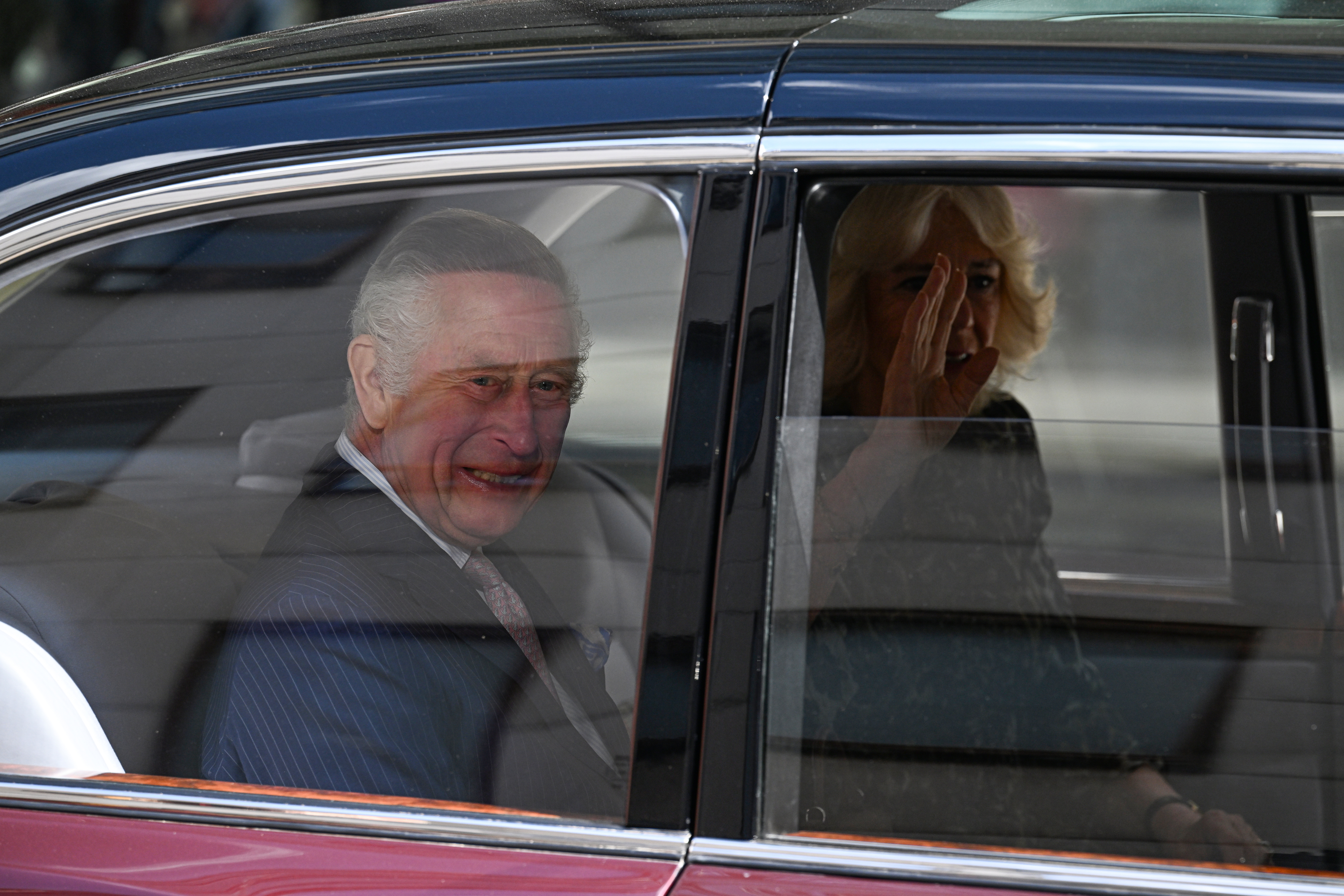 Two individuals smiling inside a car, visible through the window