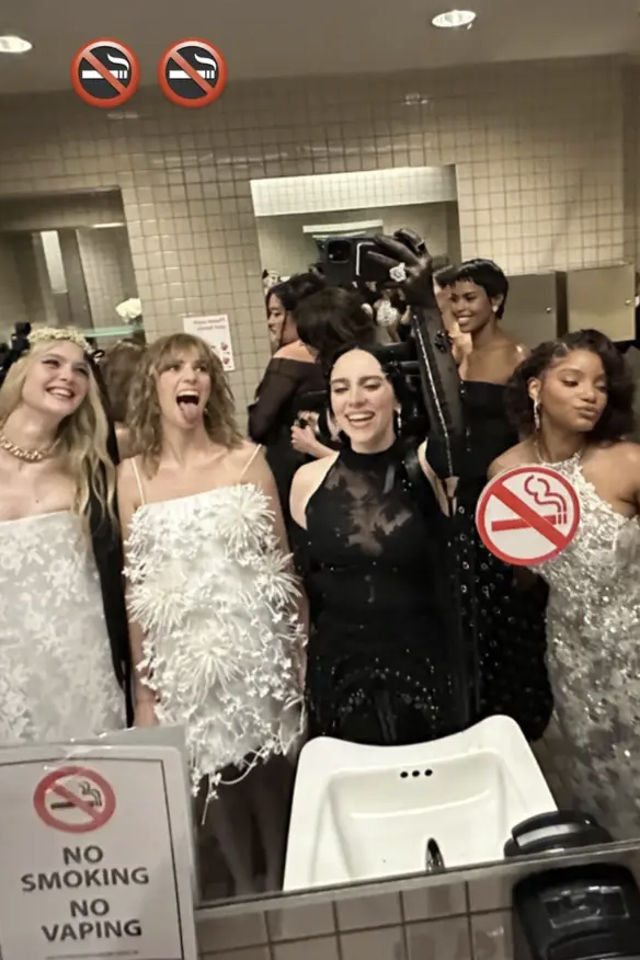 Elle, Maya, Billie, and Halle in elegant attire taking a mirror selfie in a restroom, signs indicating no smoking or vaping present