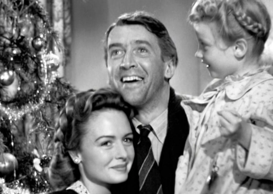 A black and white movie still showing a man embracing a woman and a child beside a Christmas tree