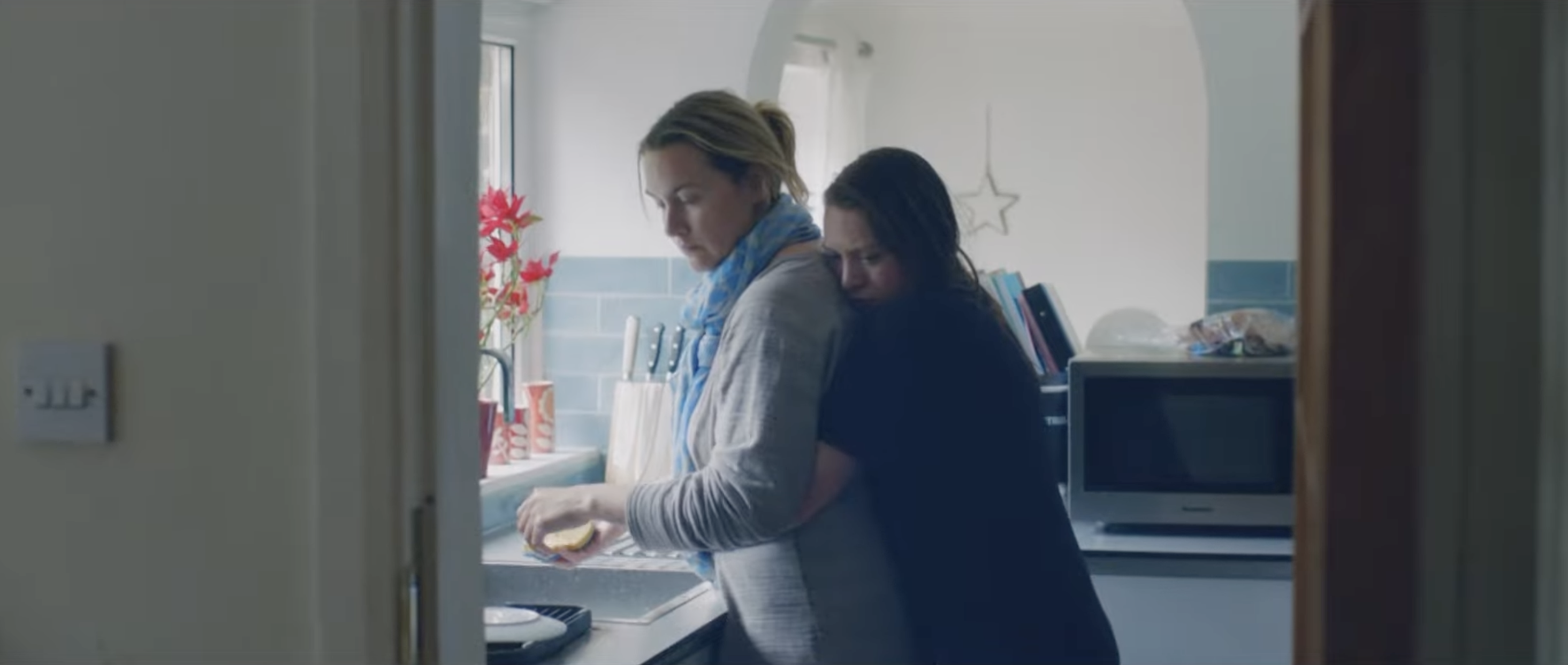 Two women embracing in a kitchen, one appears to be consoling the other