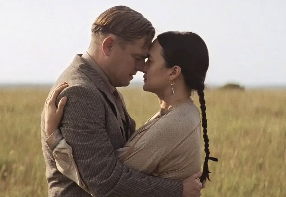 Two characters from a film are embracing in a field, showing a moment of emotional connection