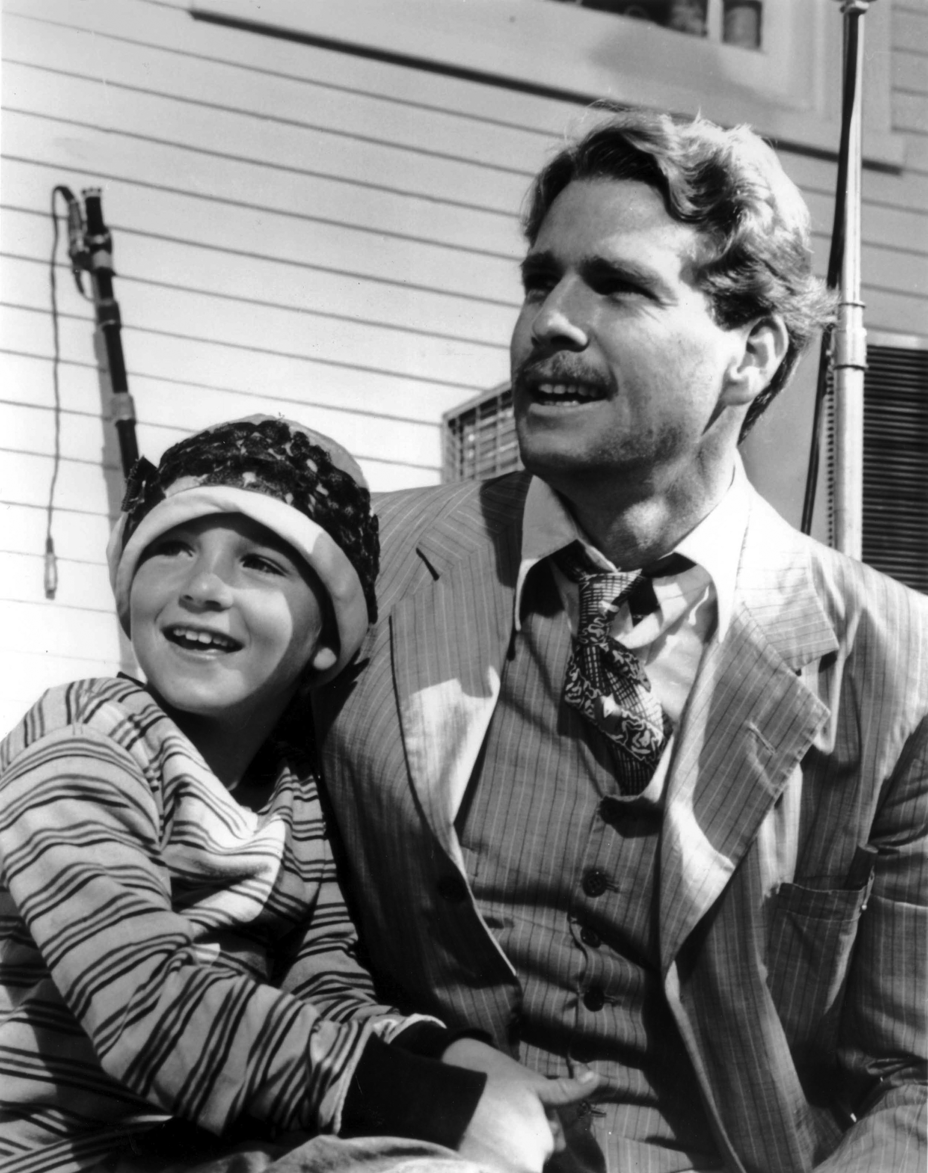 Man and boy smiling, boy in cap and striped outfit, man in patterned suit, standing outdoors