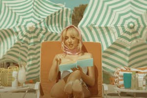 Woman lounging on a chair reading a book, surrounded by beach umbrellas and sun care products