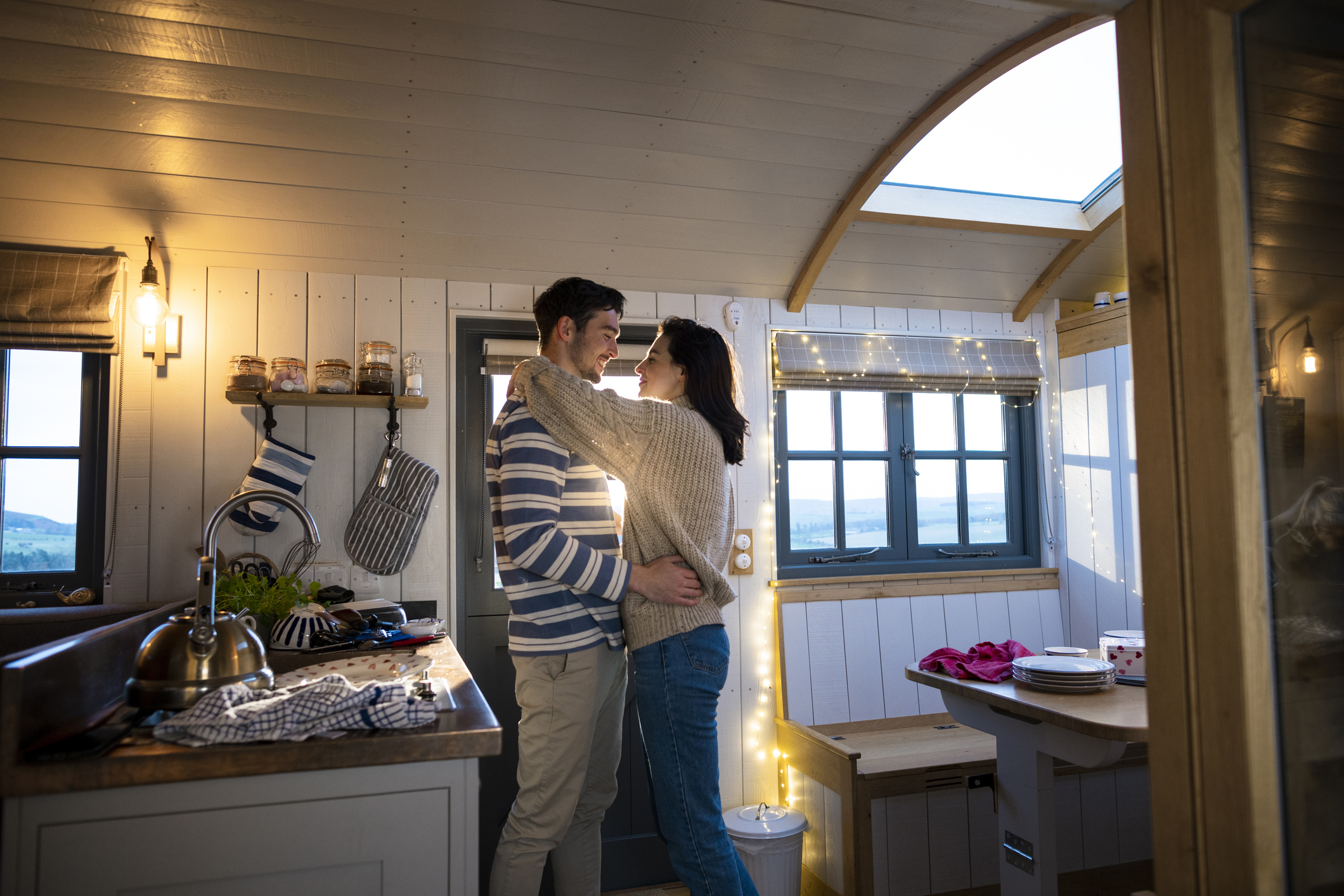 Couple embracing in a cozy tiny house kitchen with string lights, showing affection