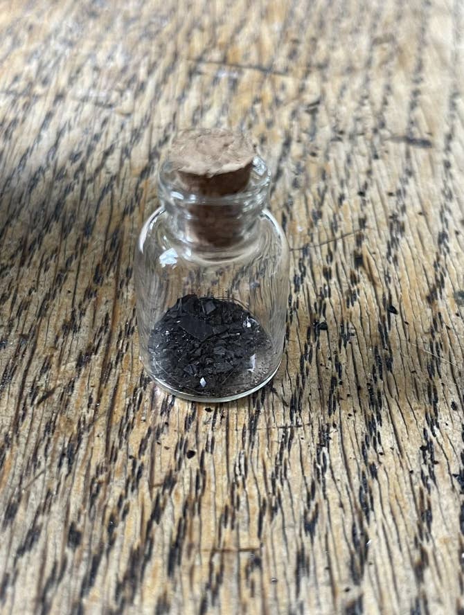 Small glass bottle with a cork, containing black granular substance, on a wooden surface