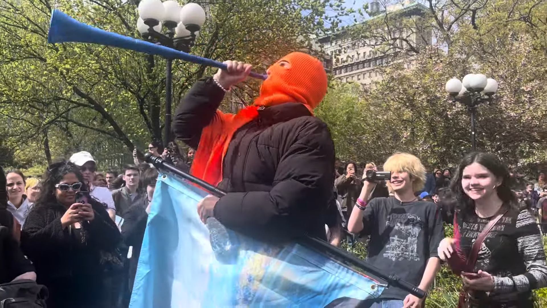 Cheeseballman in orange ski mask and black jacket, surrounded by onlookers