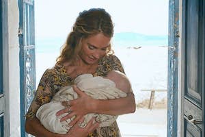 Woman holding a newborn baby, standing in a doorway with ocean view in the background