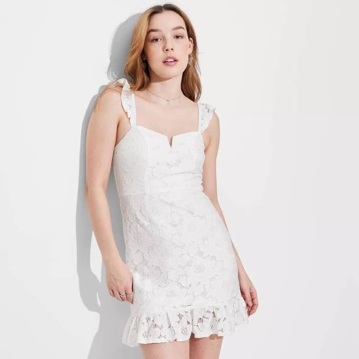Person wearing a sleeveless white lace dress with a ruffled hem