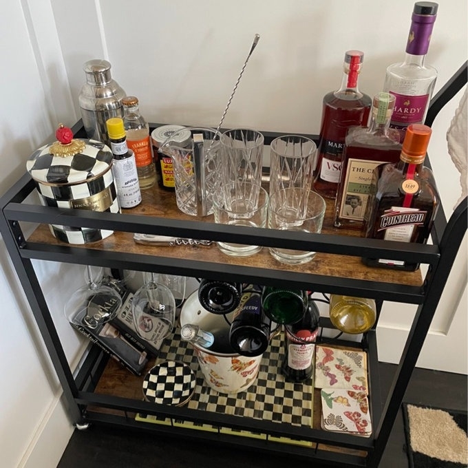 A home bar cart with various bottles, glasses, and cocktail-making accessories on shelves