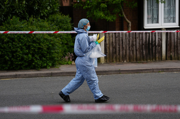 Person in protective gear walking by a taped-off area, carrying items